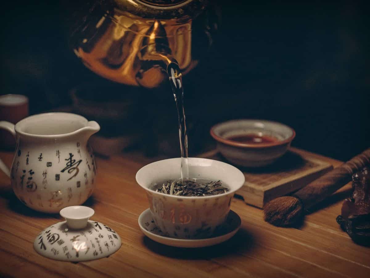 Tea being poured from a gold kettle into a gaiwan during a tea ceremony